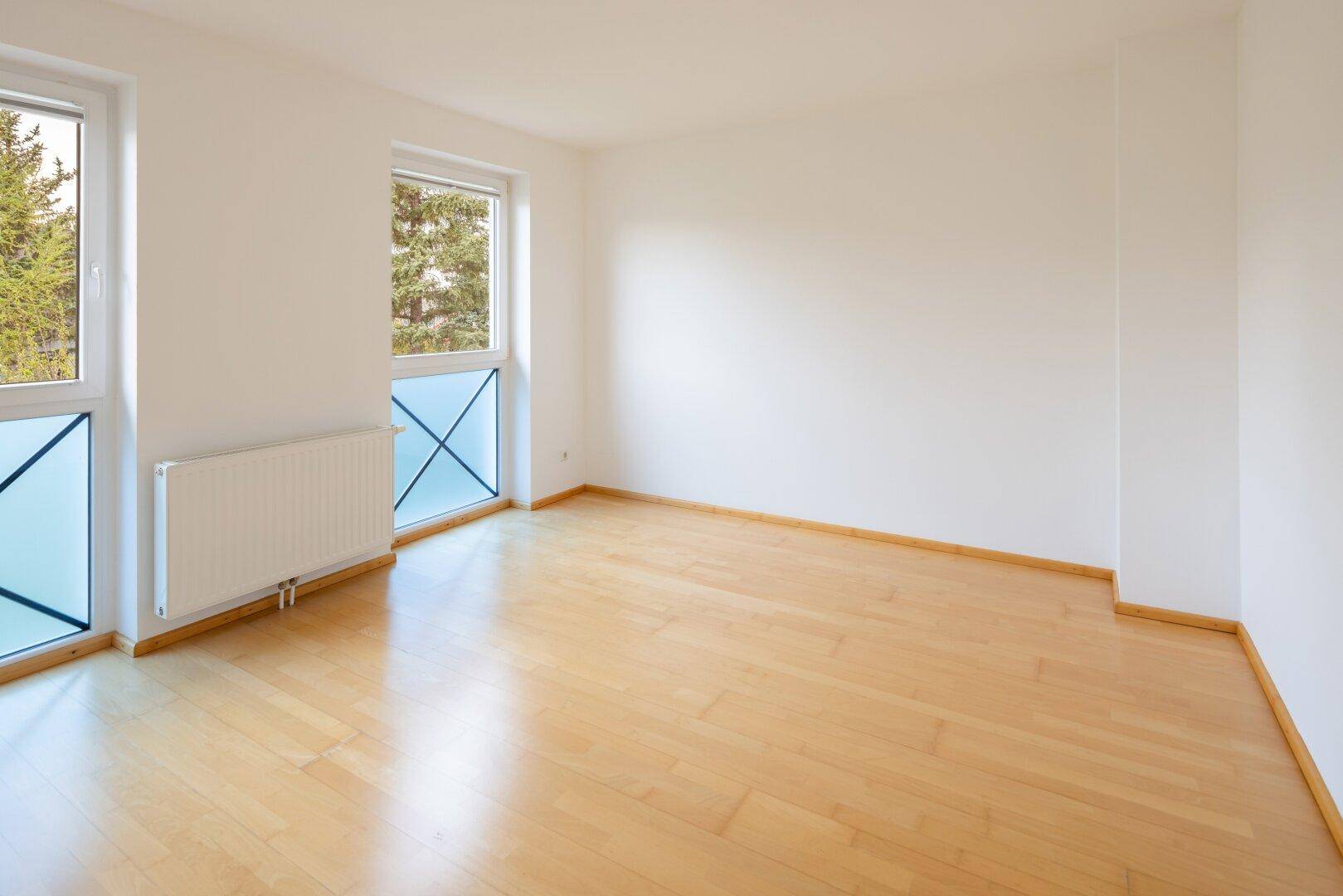 Heller Raum mit Holzfußboden und zwei Fenstern, die viel Tageslicht hereinlassen.