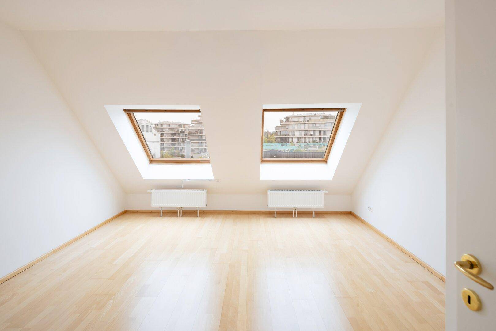 Helles Dachzimmer mit Holzfußboden und zwei Dachfenstern, ideal als Schlafzimmer.