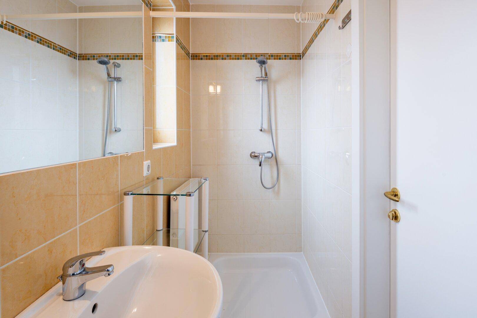 Gefliestes Badezimmer mit Dusche, Einzelwaschbecken und Spiegel.
