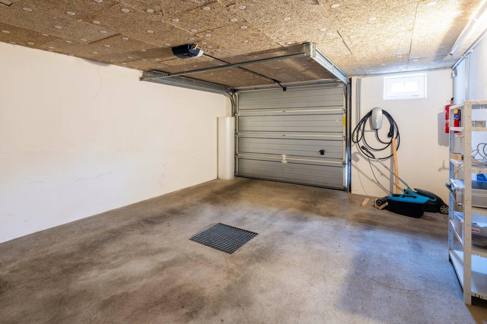Geräumige Garage im Untergeschoss mit Betonboden, Sektionaltor und einer EV-Ladestation.