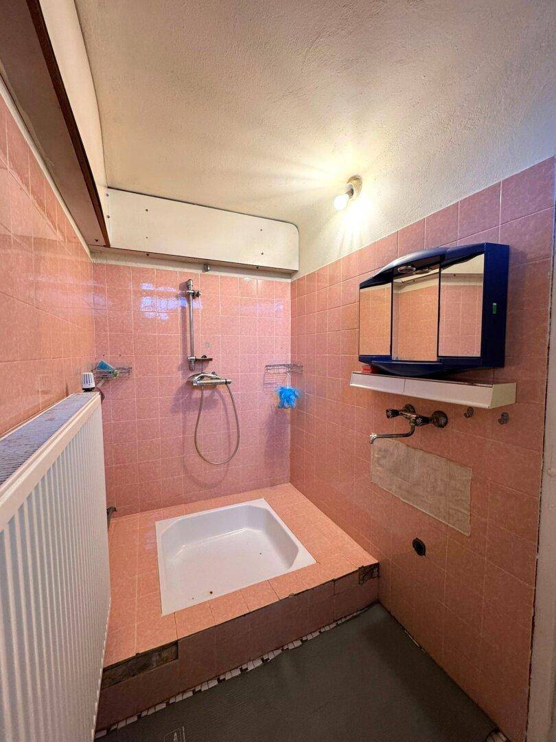 Kleines Badezimmer mit rosa Fliesen, Duschwanne und Spiegelschrank.