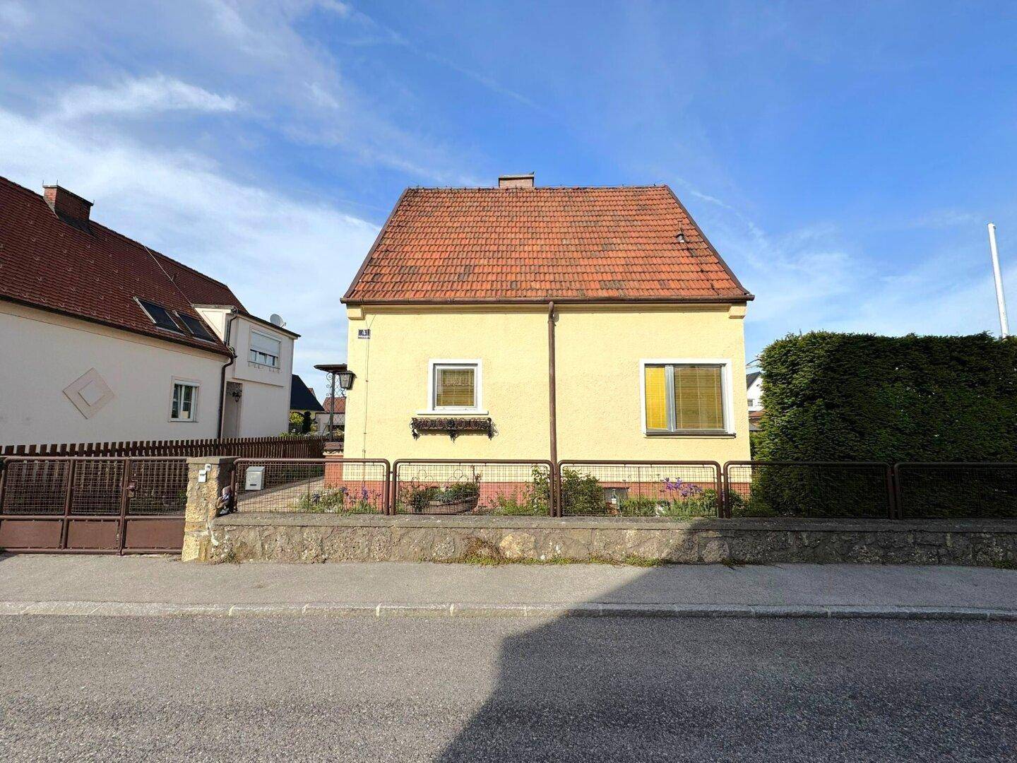 Vorderansicht des Einfamilienhauses mit gelber Fassade und rotem Ziegeldach.