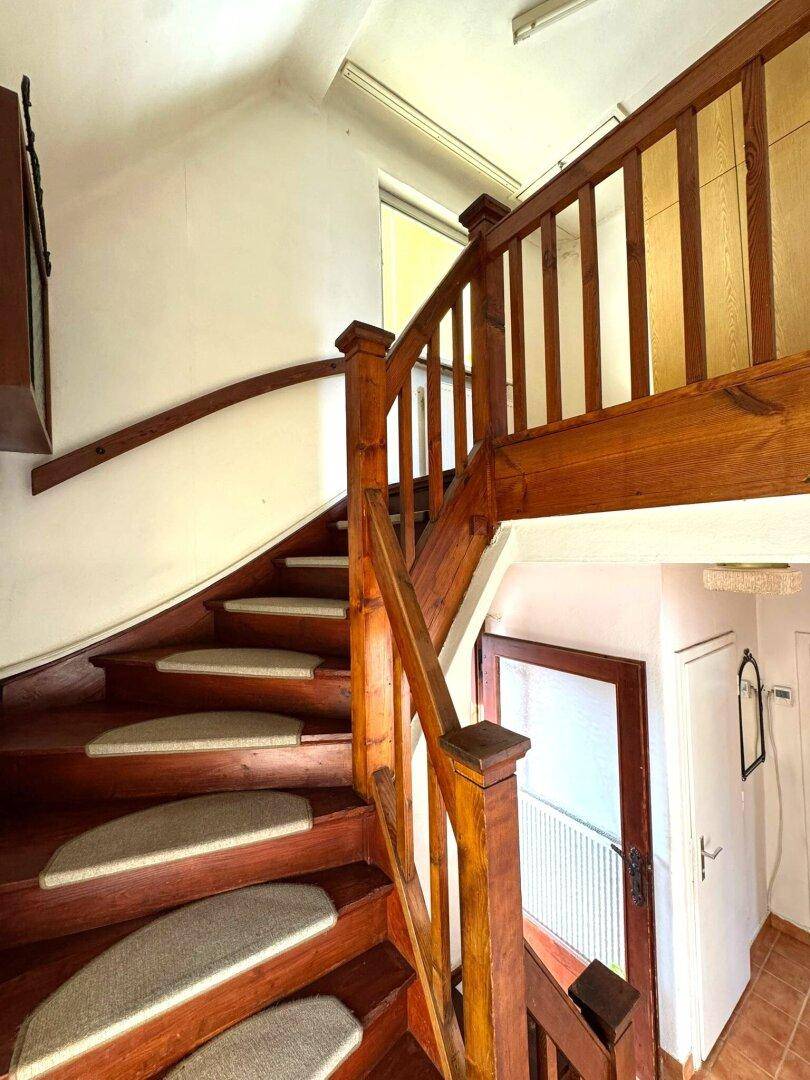 Holztreppe mit Teppichstufen und Geländer, die in die obere Etage führt.