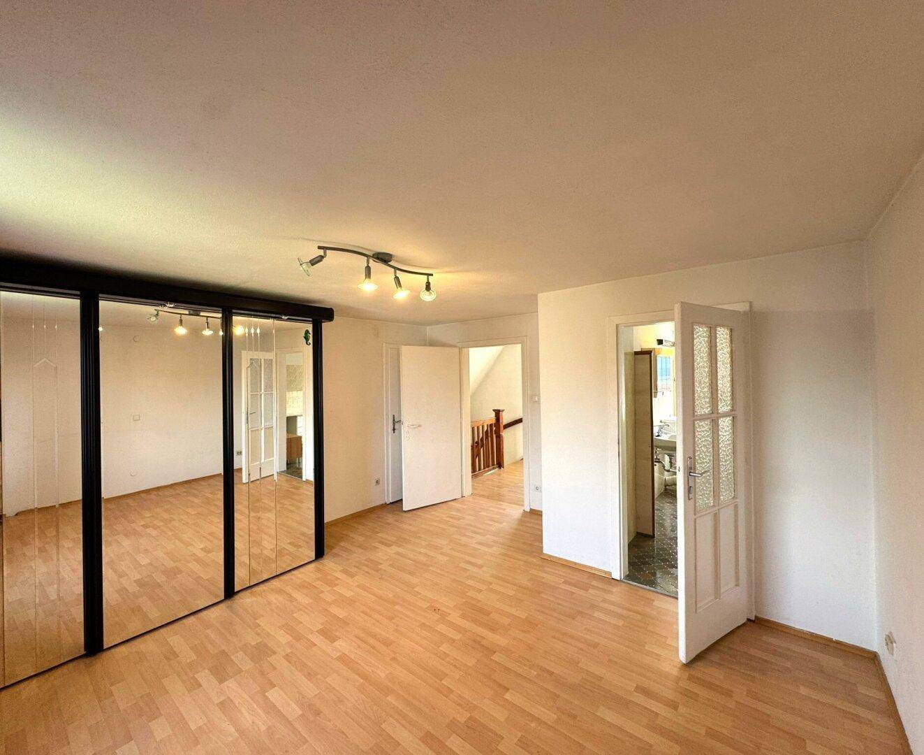 Geräumiges Schlafzimmer mit Laminatboden und großem Spiegelschrank.