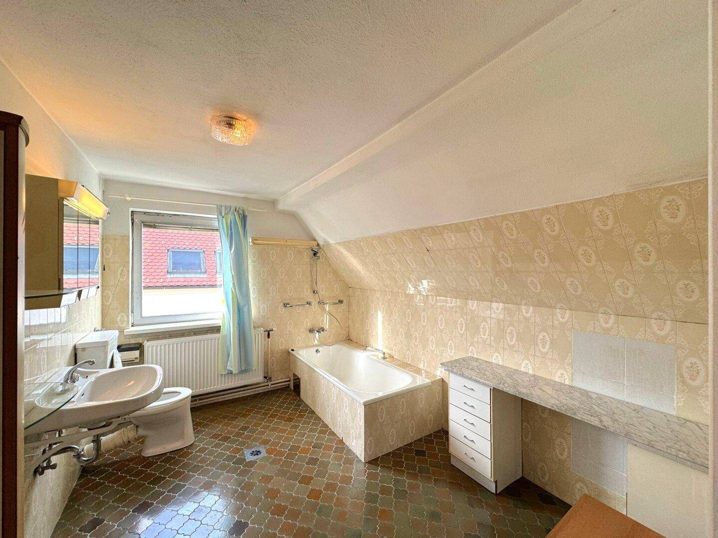 Badezimmer im Dachgeschoss mit Badewanne, Waschbecken und Fenster.
