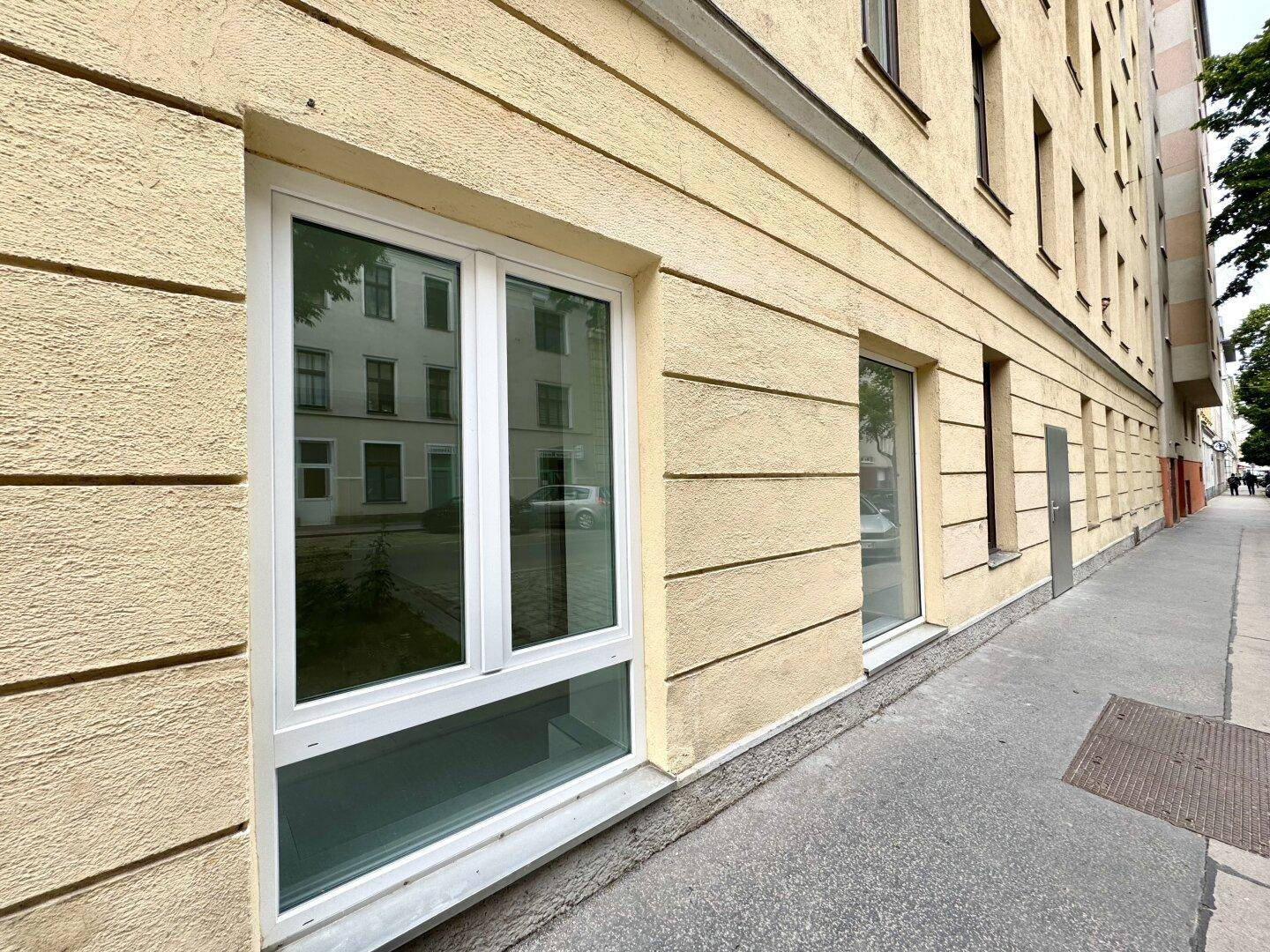 Detailansicht der gelben Fassade mit neuen, weißen Fenstern und strukturierter Oberfläche im Erdgeschoss.