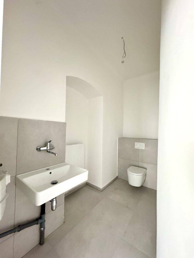 Modernes WC mit Wand-WC, Waschbecken und hellen Fliesen an Wänden und Boden.