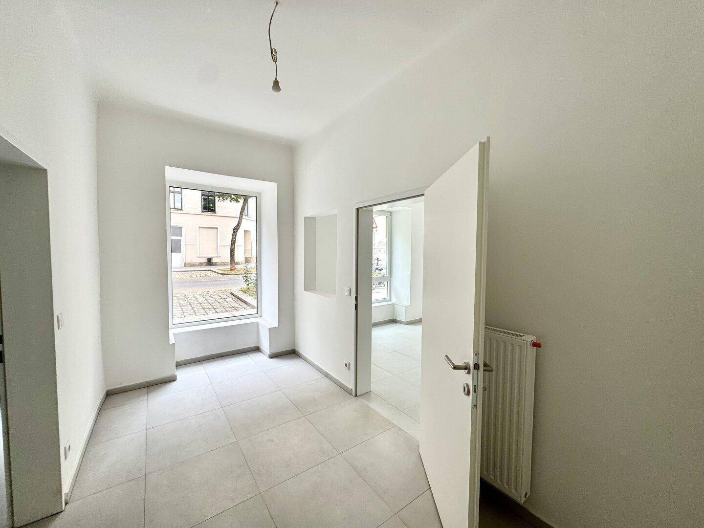 Heller Raum mit Fliesenboden und großem Fenster, das viel Tageslicht hereinlässt.