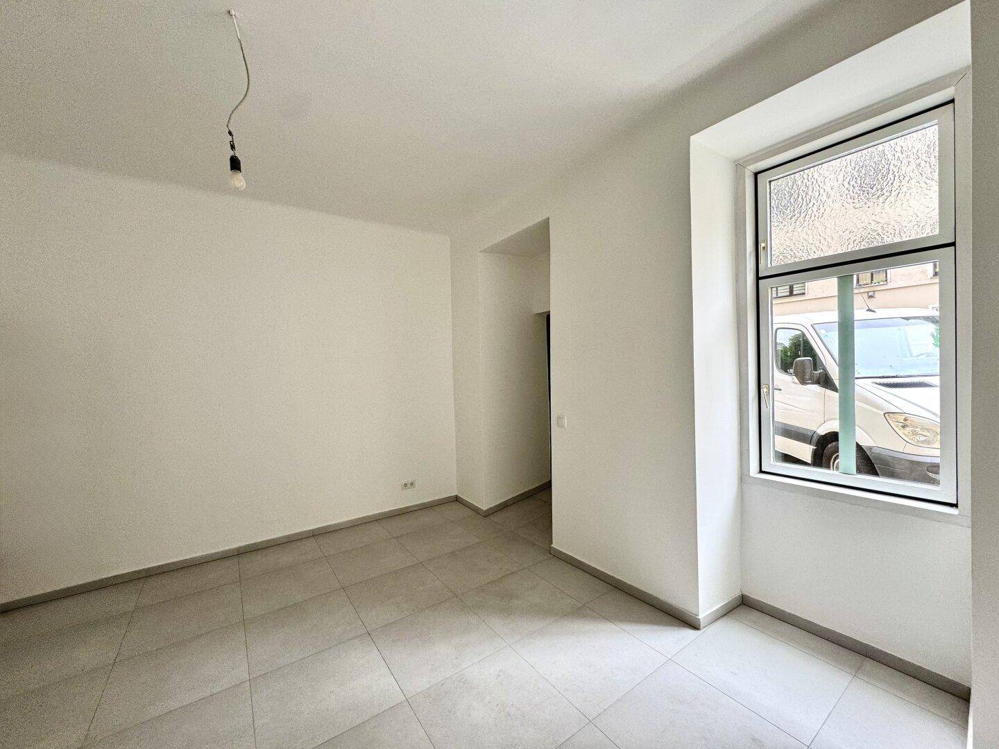 Kleinerer, heller Raum mit Fliesenboden und einem Fenster, das auf die Straße blickt.