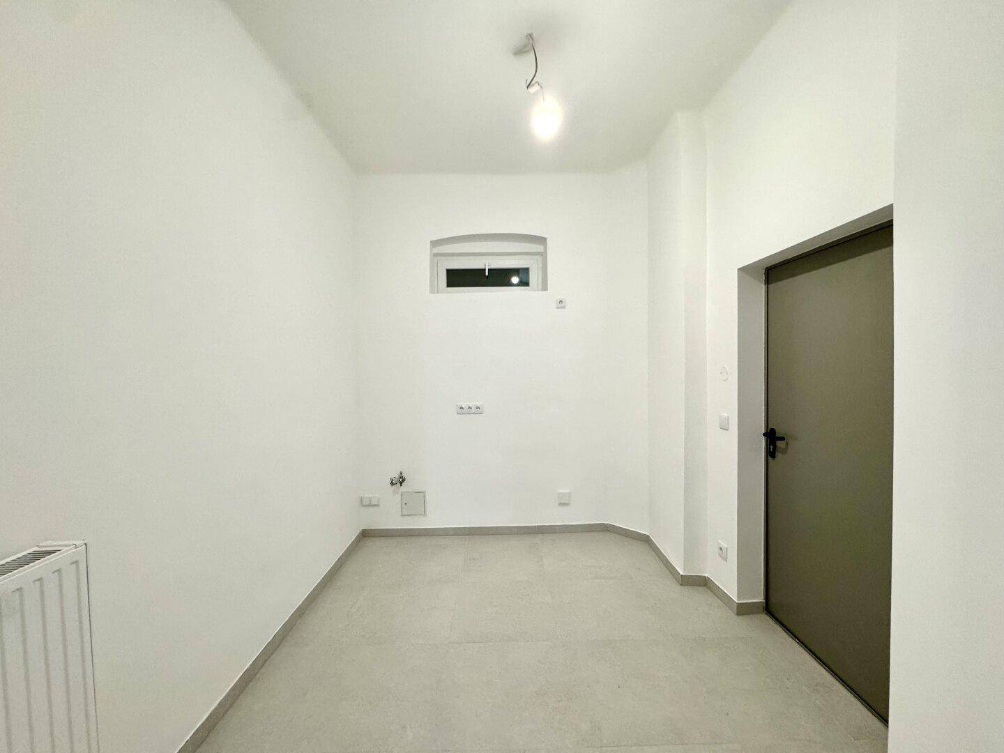 Kleiner, heller Raum mit Fliesenboden und einem hohen Fenster, ideal als Abstell- oder Hauswirtschaftsraum.