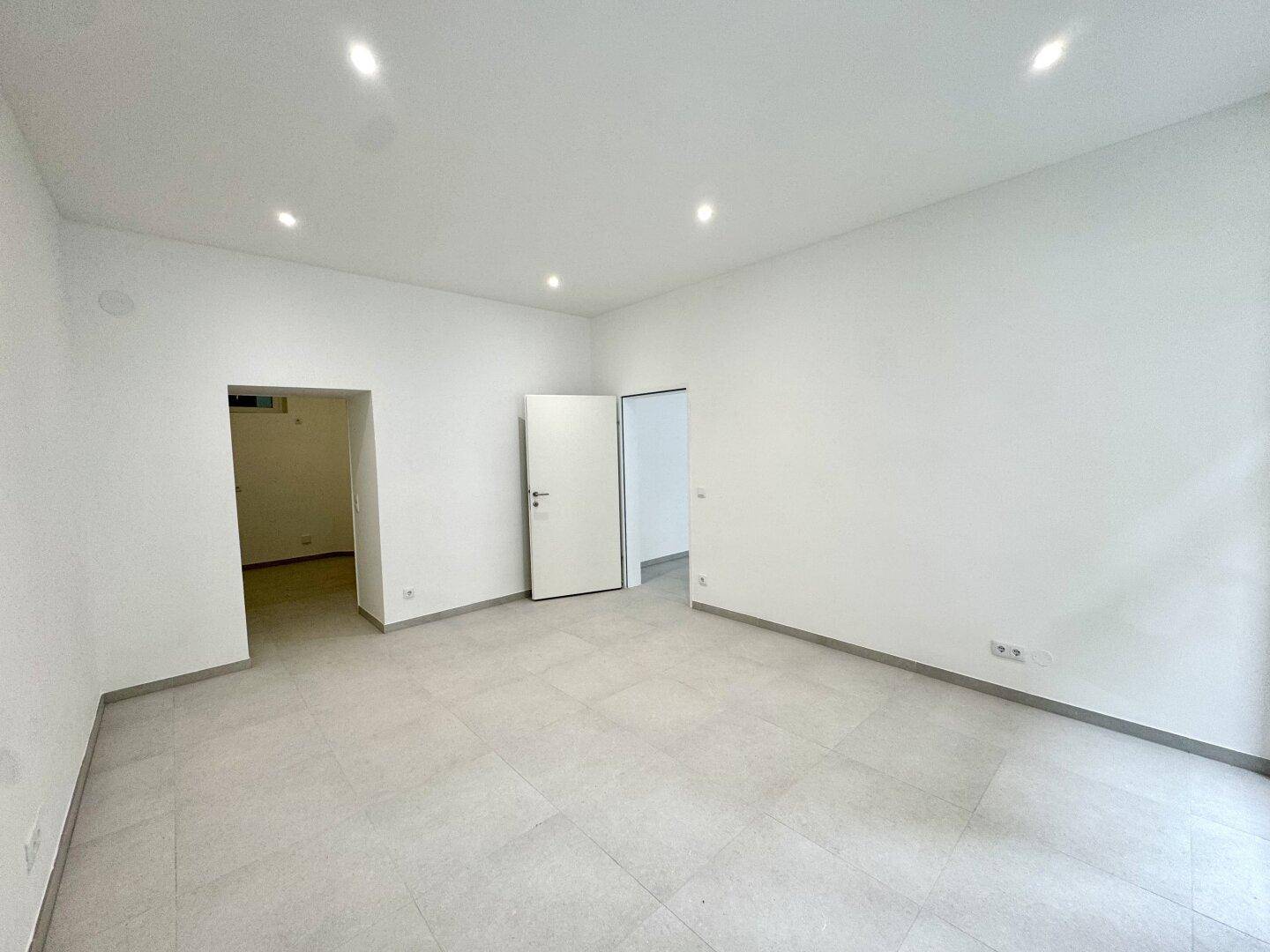 Geräumiger, heller Raum mit Fliesenboden und offenen Durchgängen zu weiteren Bereichen der Wohnung.