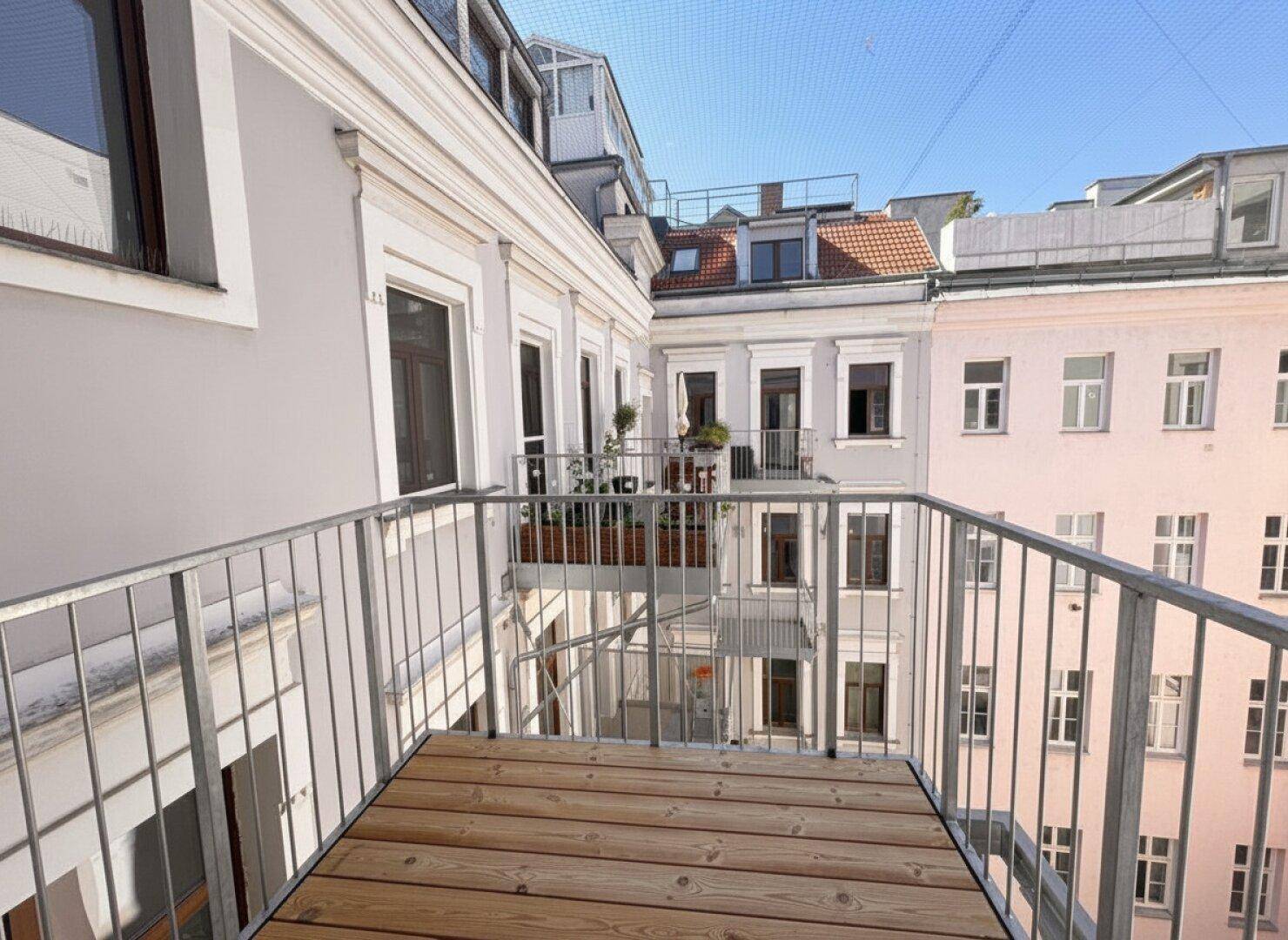 Balkon mit Holzboden und Metallgeländer, bietet einen Blick auf den Innenhof.