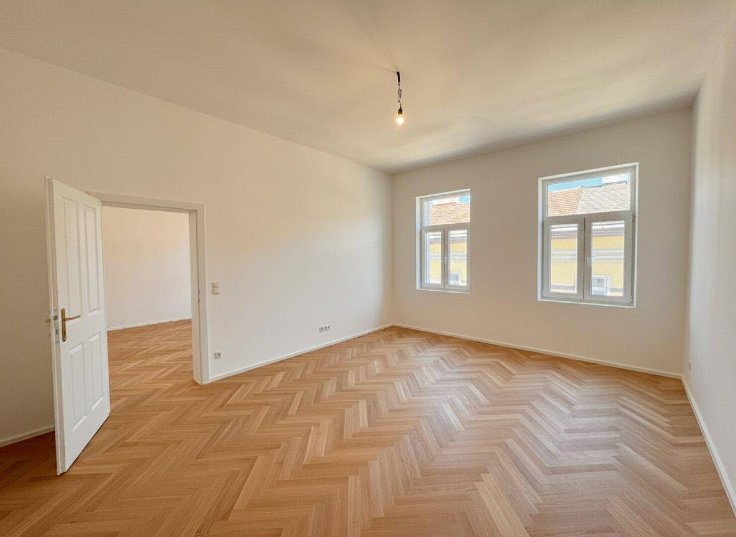 Heller Raum mit Fischgrätparkett und offener Tür zu einem angrenzenden Zimmer.