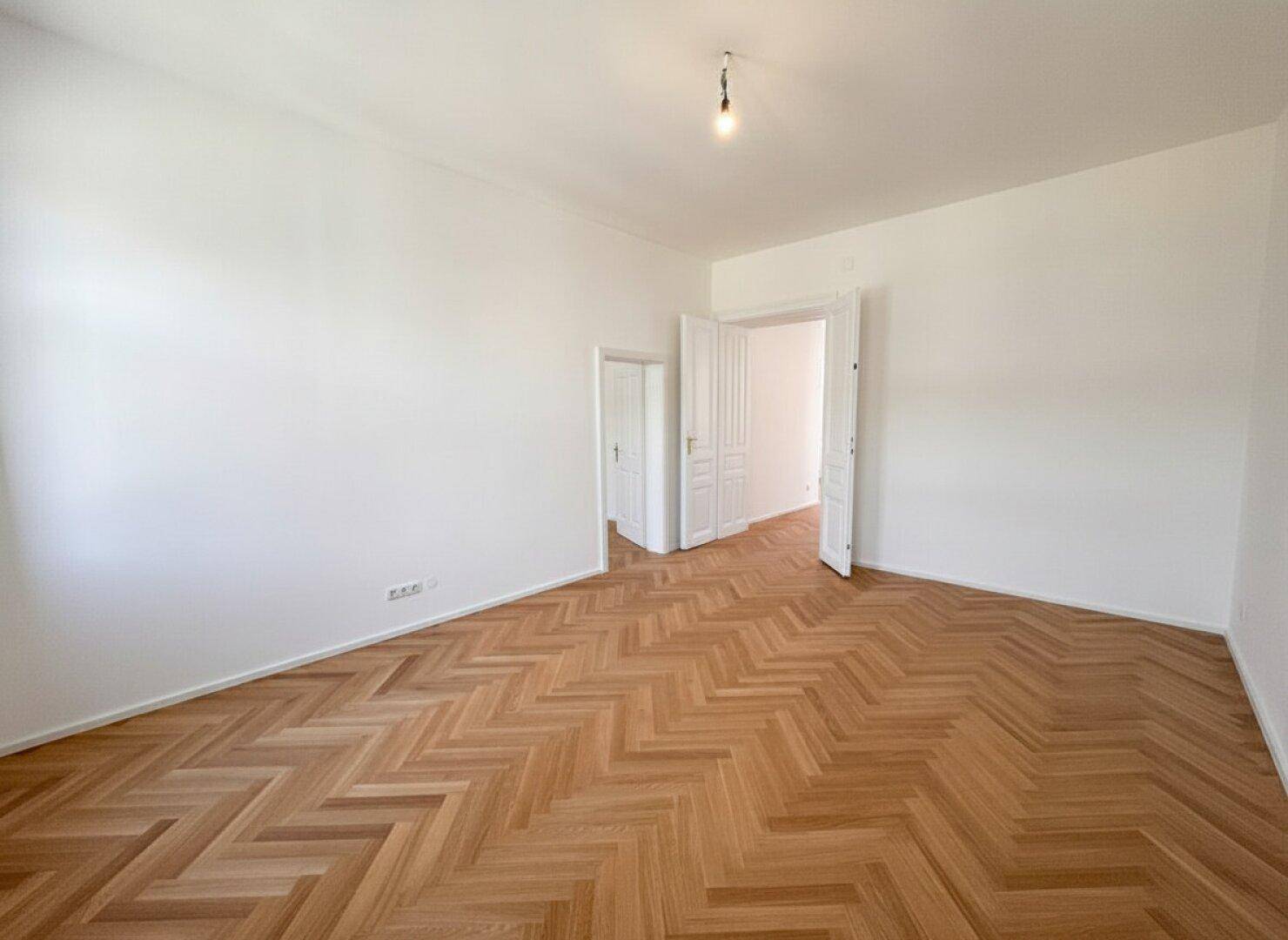 Geräumiger Raum mit Fischgrätparkett und mehreren Türen, bietet flexible Nutzungsmöglichkeiten.