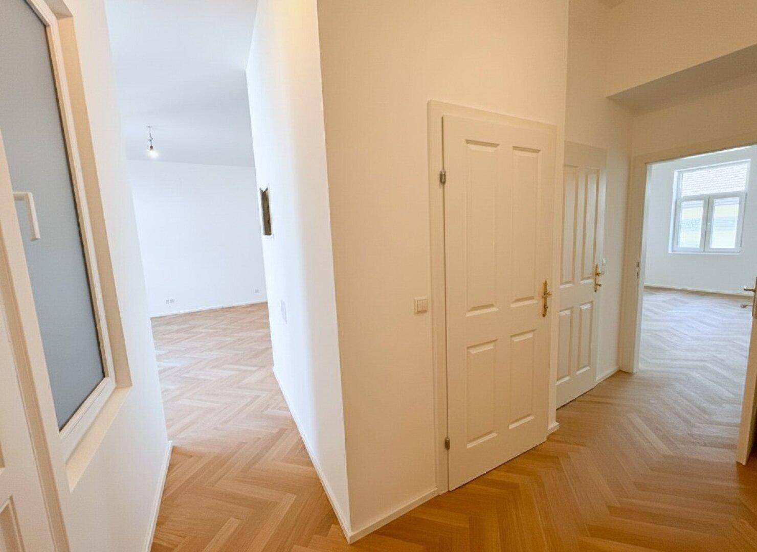 Heller Flur mit Fischgrätparkett und weißen Wänden, verbindet die verschiedenen Räume.