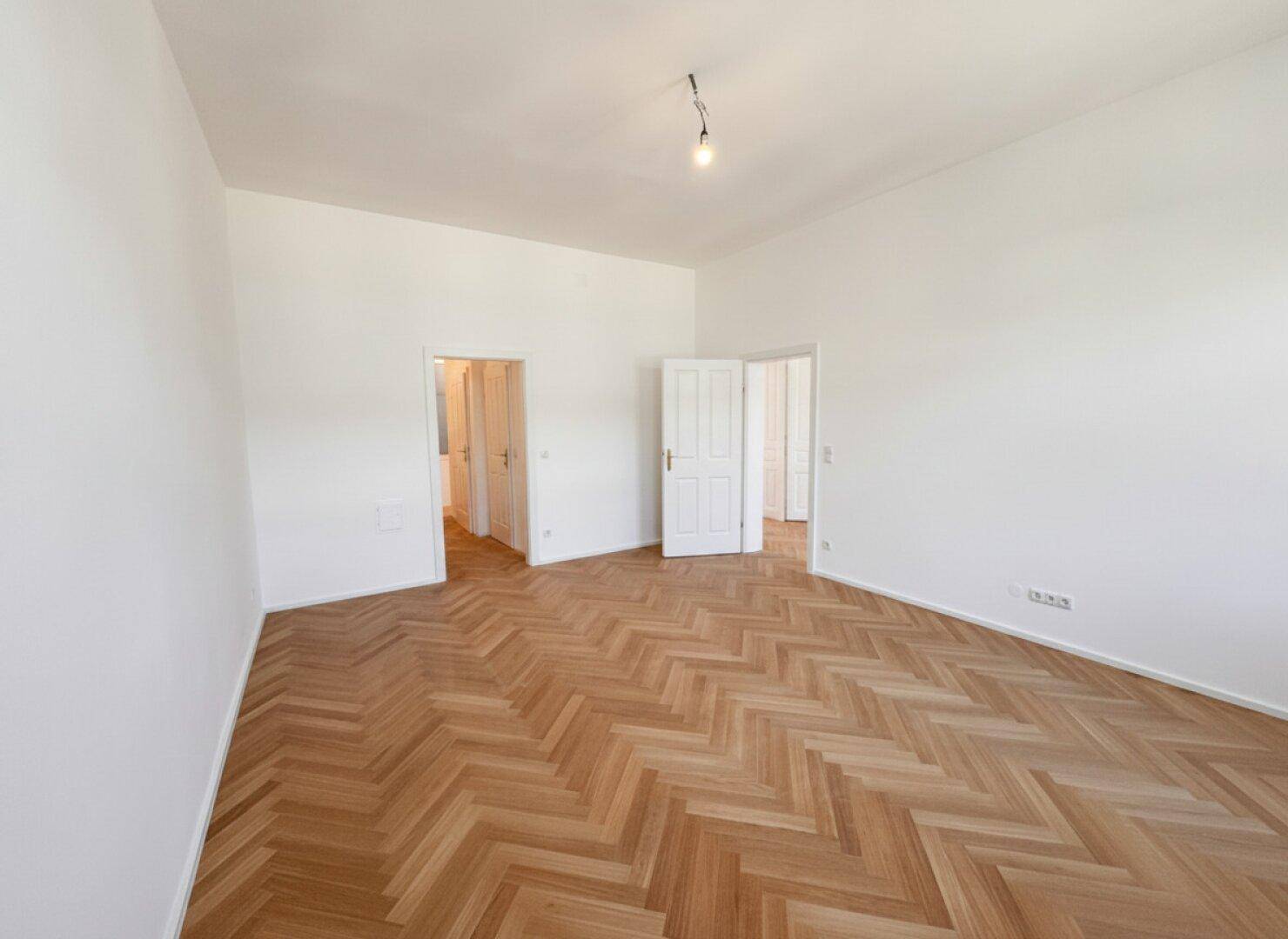 Geräumiger Raum mit Fischgrätparkett und mehreren Türen, ideal für flexible Raumgestaltung.
