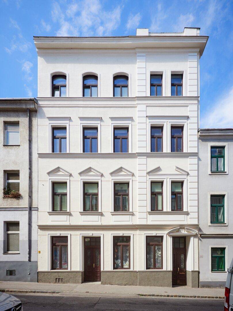 Klassische Altbaufassade mit eleganten Fenstern und Verzierungen unter blauem Himmel.