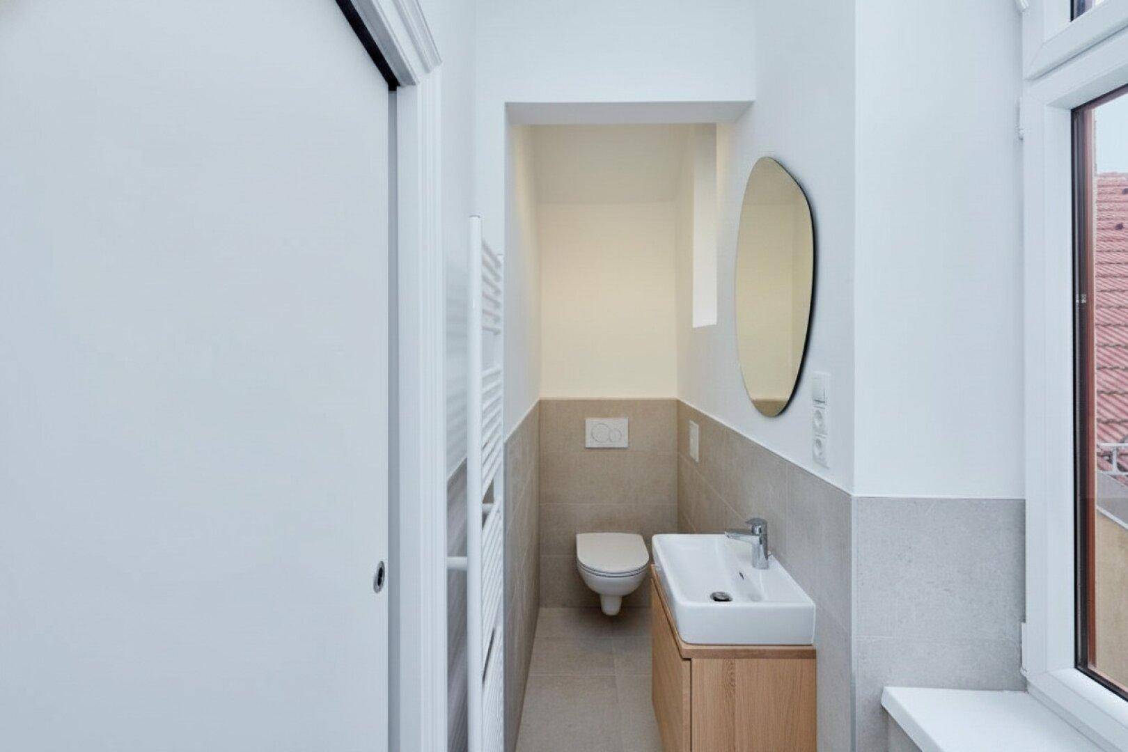 Modernes Gäste-WC mit Holzunterschrank, ovalem Spiegel und Fenster, stilvoll und praktisch.