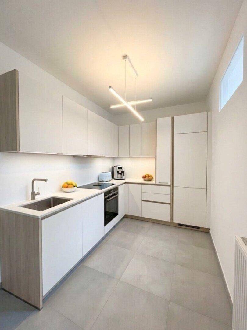 Moderne Einbauküche mit weißen Fronten, integrierten Geräten und Fliesenboden, ideal für kulinarische Erlebnisse.