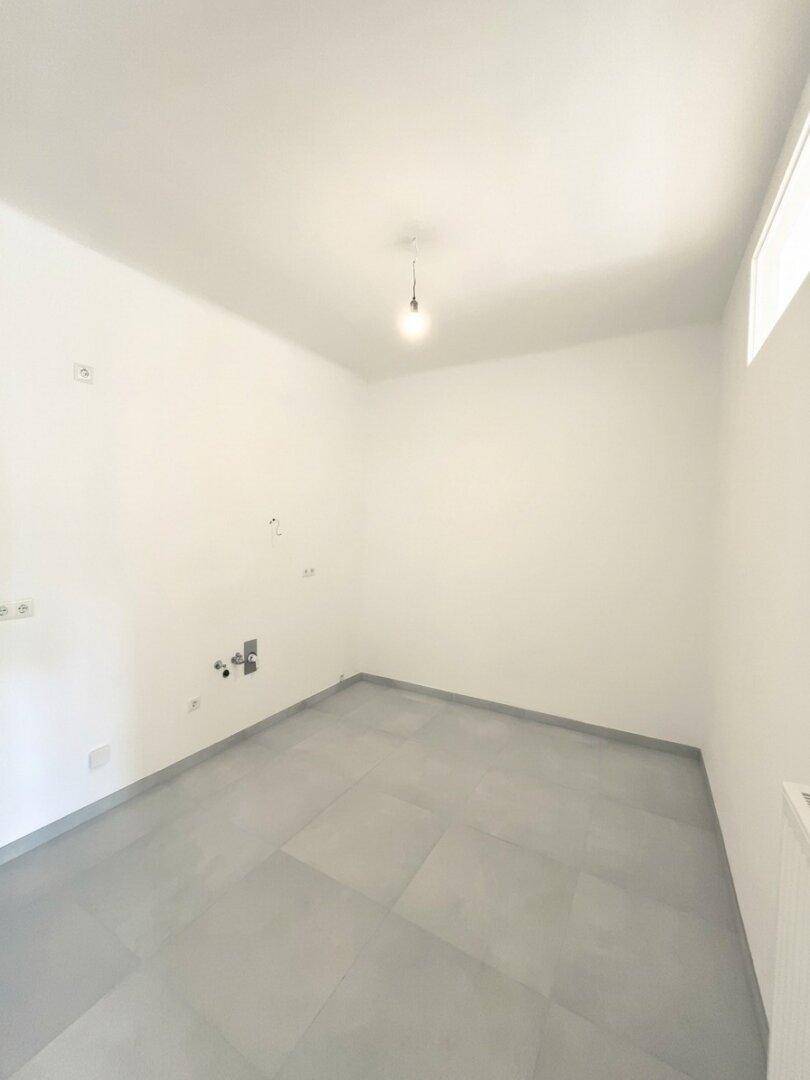Leerer Küchenraum mit Fliesenboden und Anschlüssen, bereit für eine neue, maßgeschneiderte Einbauküche.