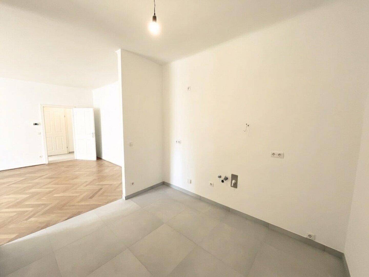 Unmöblierter Küchenbereich mit Fliesenboden und vorbereiteten Anschlüssen für die Kücheninstallation.
