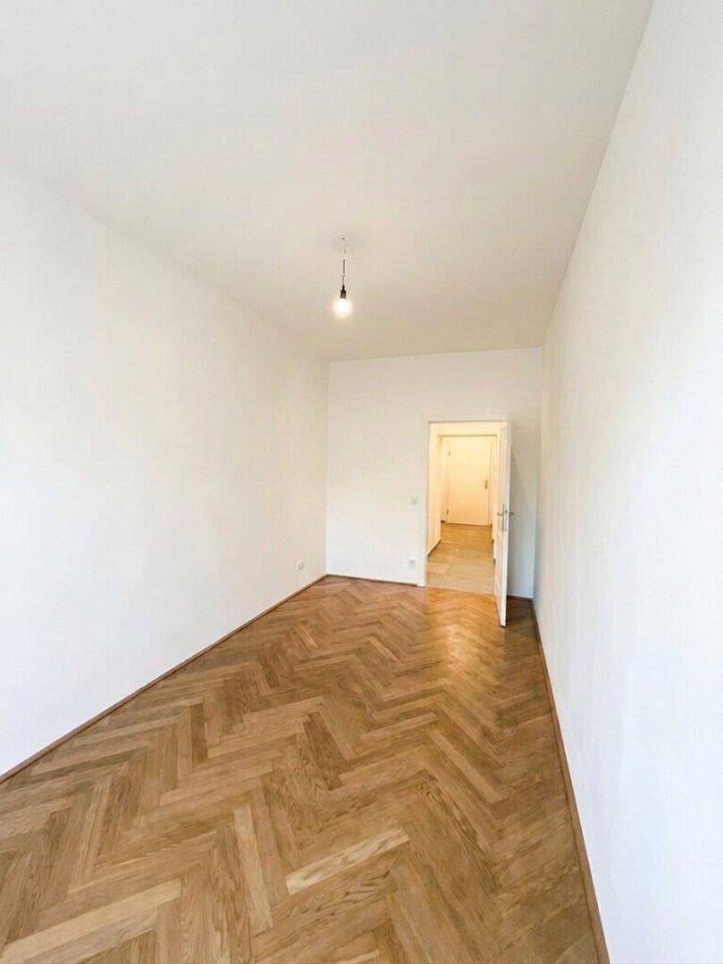 Geräumiges, unmöbliertes Schlafzimmer mit Fischgrätparkett und weiß gestrichenen Wänden, bereit zur Einrichtung.