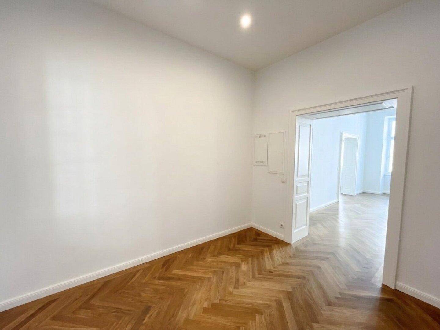Heller Flur mit Fischgrätparkett und Zugang zu weiteren Räumen, gut beleuchtet und einladend.