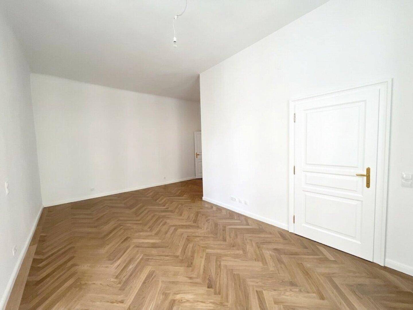 Helles Wohnzimmer mit Fischgrätparkett und hohen Decken, ideal für offenes Wohnen und viel Platz.