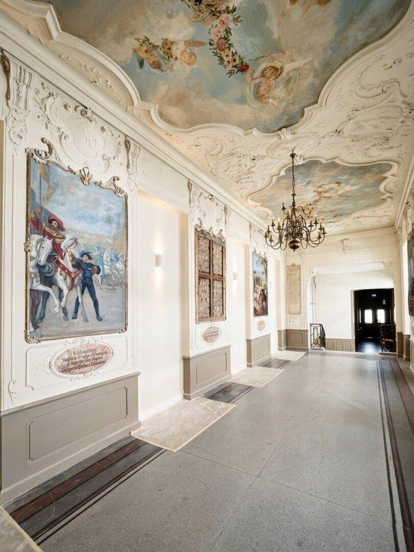Prunkvoller Flur mit kunstvollen Deckenmalereien, Stuckverzierungen und Kronleuchter.