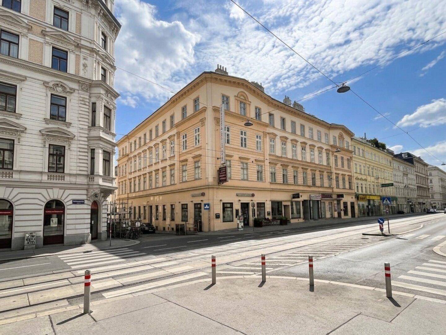 Historisches Eckgebäude an einer Kreuzung in der Stadt mit klassischer Architektur und Geschäften im Erdgeschoss.