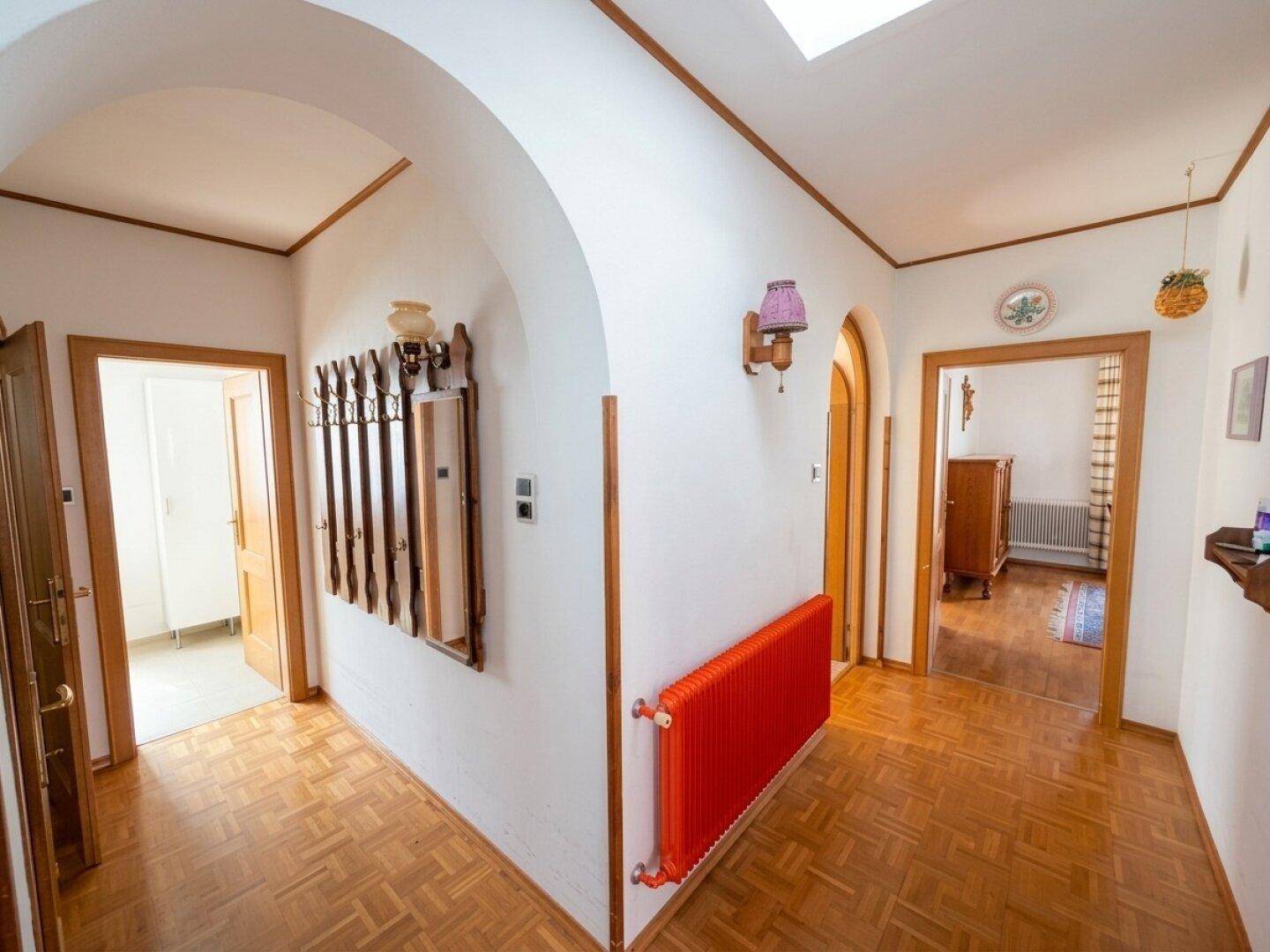 Heller Flur mit Parkettboden, Holztüren und einem auffälligen roten Heizkörper.