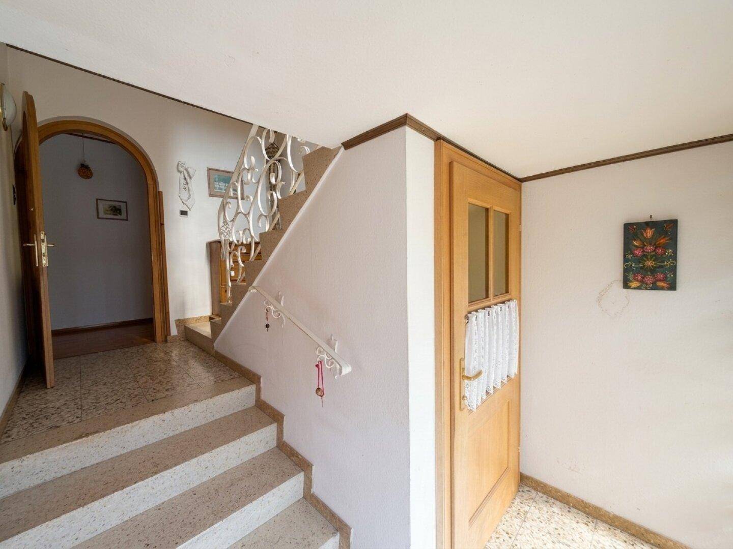 Eingangsbereich mit Steintreppe, schmiedeeisernem Geländer und Holztür.