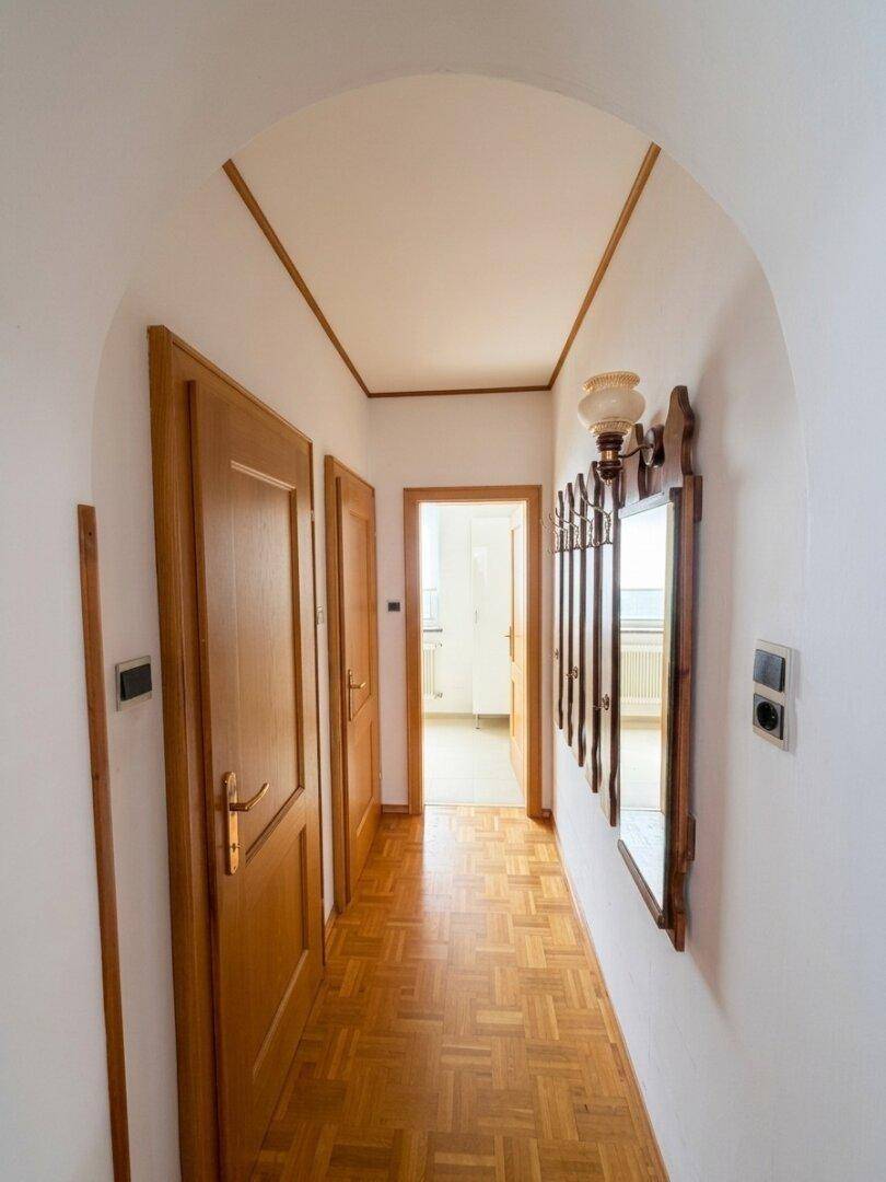 Langer Flur mit Parkettboden, Holztüren und einem Spiegel an der Wand.