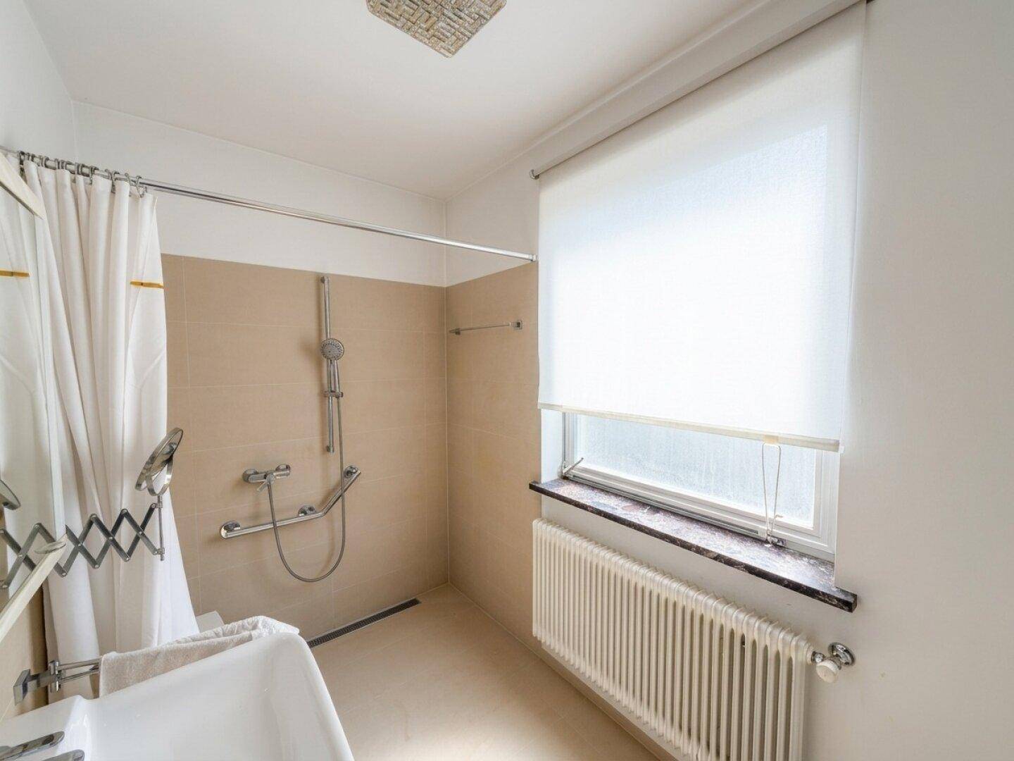 Badezimmer mit ebenerdiger Dusche, Fenster und Heizkörper, hell und funktional.