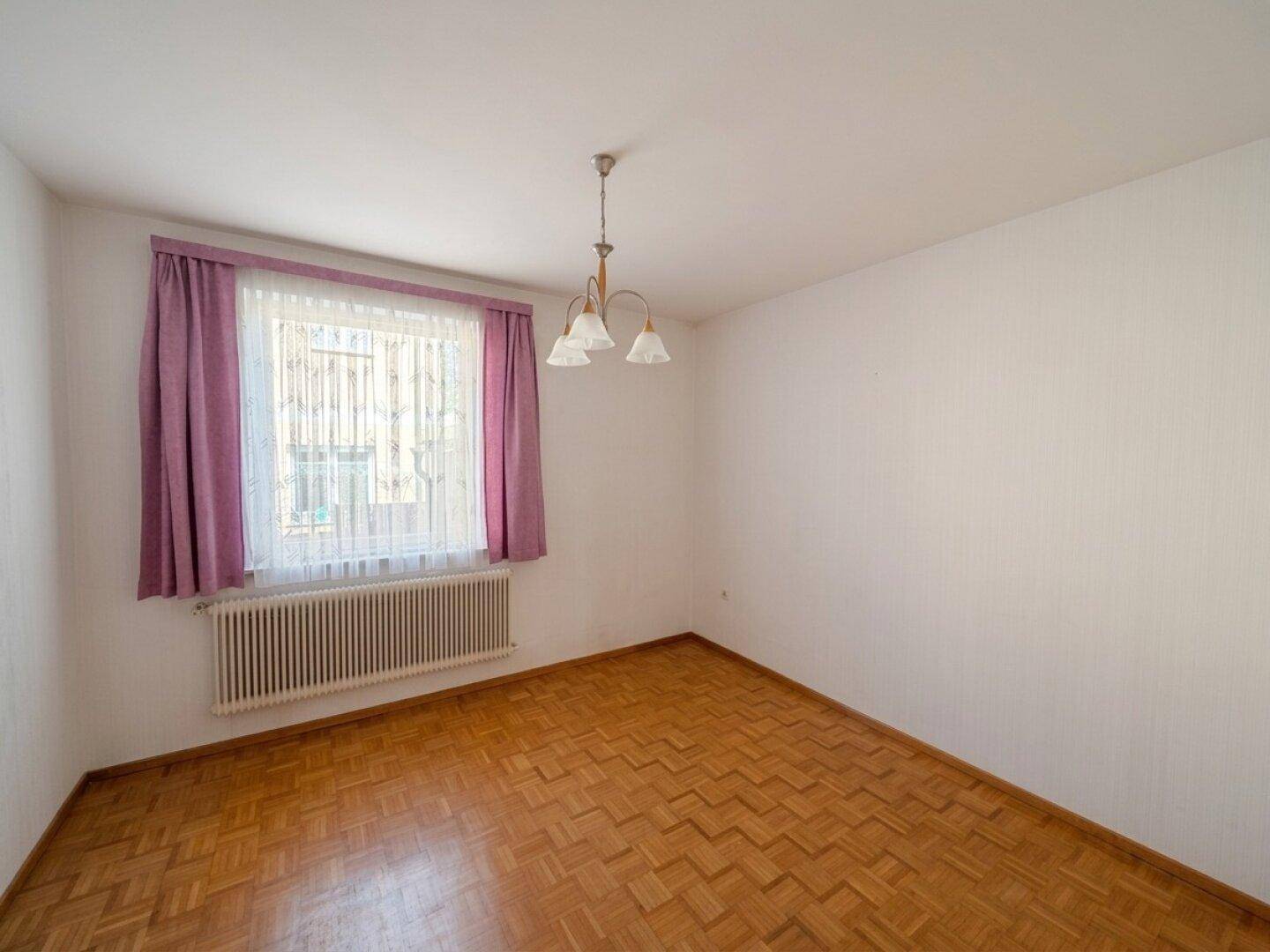 Geräumiges Zimmer mit Parkettboden, weiß gestrichenen Wänden und großem Fenster.