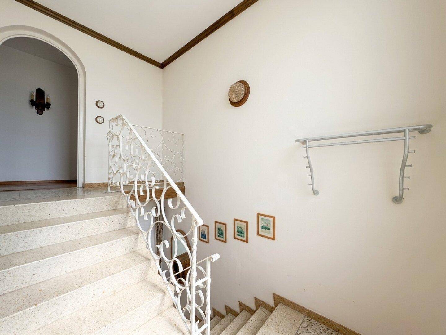 Treppenhaus mit Steinstufen, schmiedeeisernem Geländer und Garderobe.