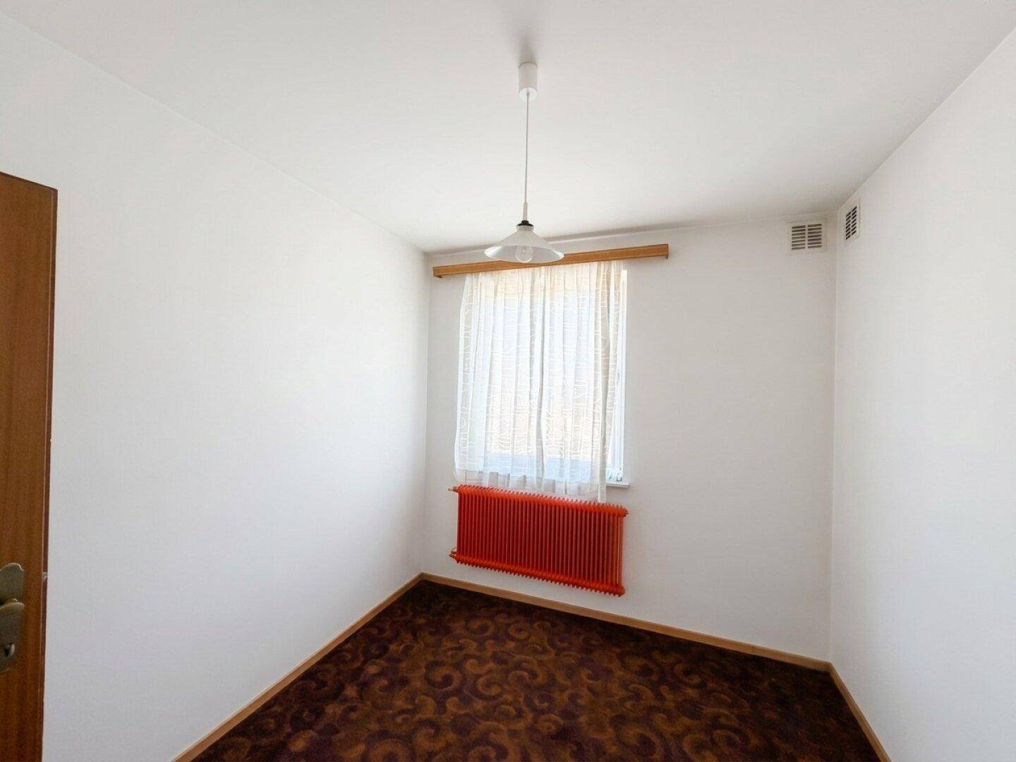 Gemütliches Schlafzimmer mit Teppichboden, Fenster und einem auffälligen roten Heizkörper.
