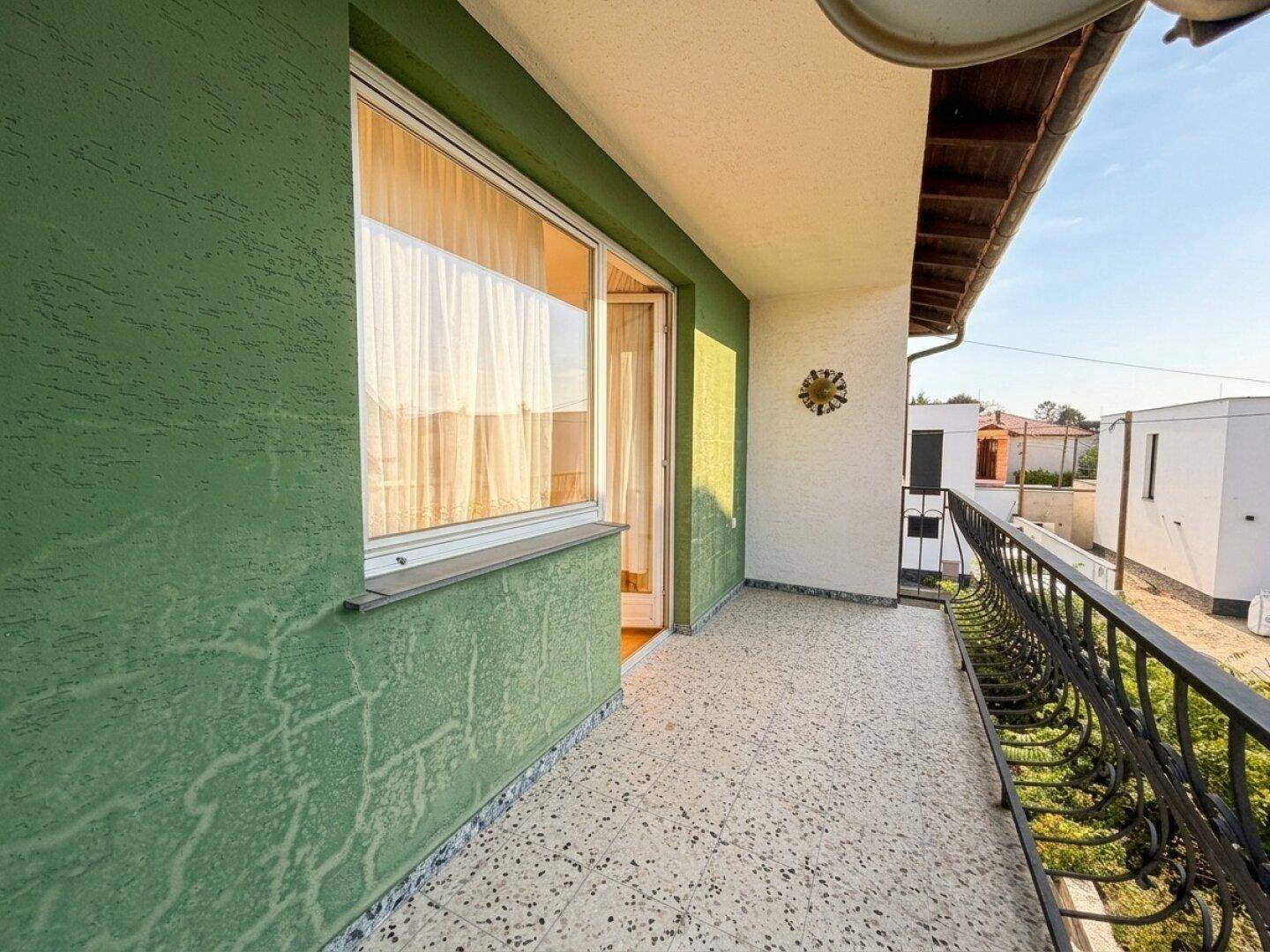 Balkon mit grün gestrichener Wand, Fliesenboden und Blick auf die Umgebung.