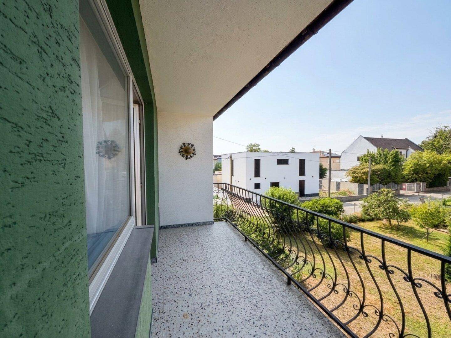 Geräumiger Balkon mit schmiedeeisernem Geländer und Blick ins Grüne.