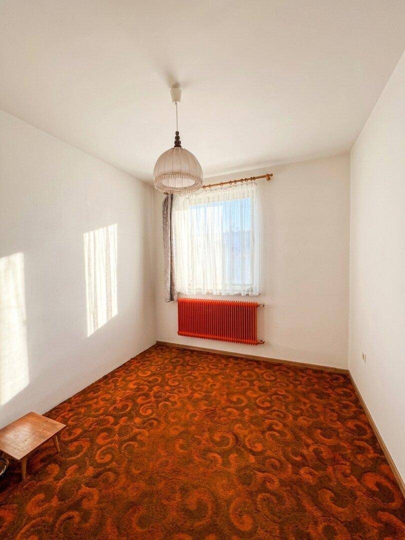Helles Schlafzimmer mit Teppichboden, rotem Heizkörper und viel Tageslicht.