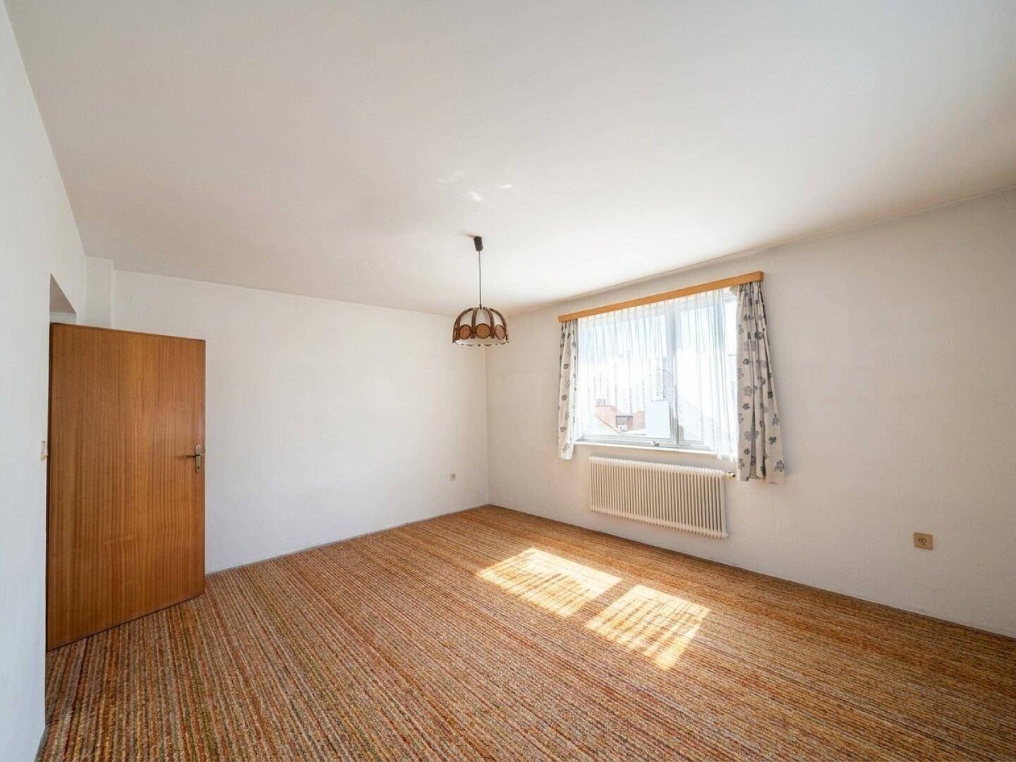 Helles Wohnzimmer mit Teppichboden, Fenster und Holztür.