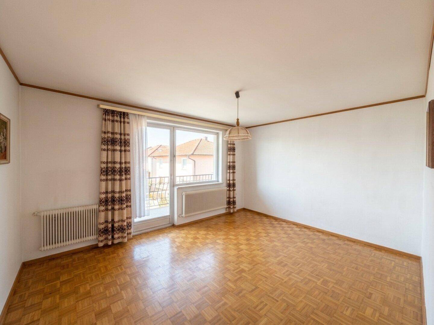 Wohnzimmer mit Parkettboden, Balkonzugang und traditionellen Vorhängen.