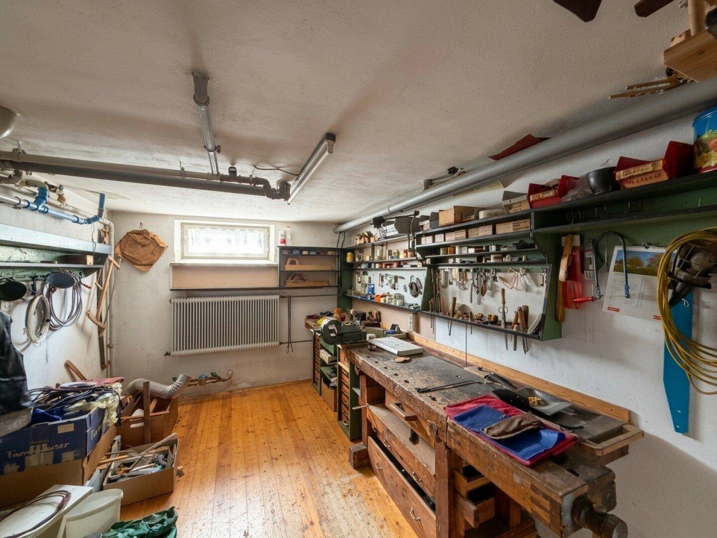 Geräumige Werkstatt im Keller mit Holzfußboden, einer großen Werkbank und vielen Regalen.