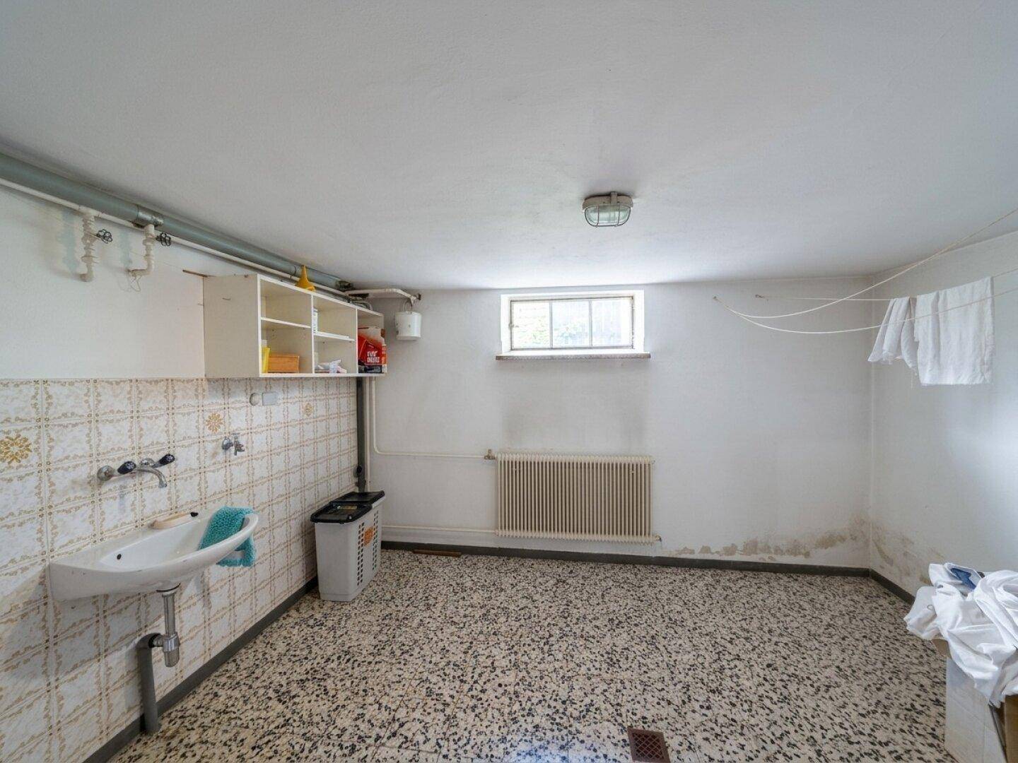 Funktionaler Waschraum im Keller mit Waschbecken, Fliesenwand und einem kleinen Fenster.