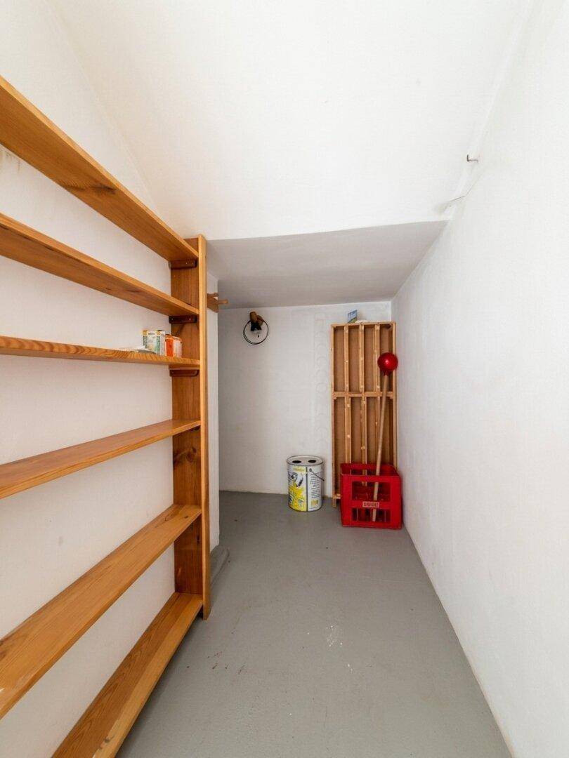 Abstellraum mit Holzregalen, grauem Boden und weiß gestrichenen Wänden.