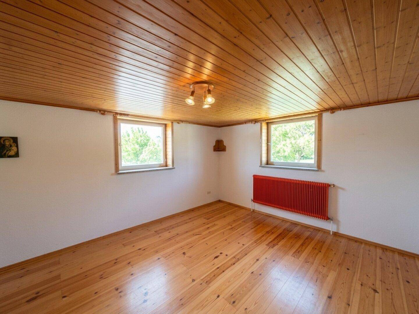 Schlafzimmer mit Holzboden, Holzdecke und zwei Fenstern mit Grünblick.