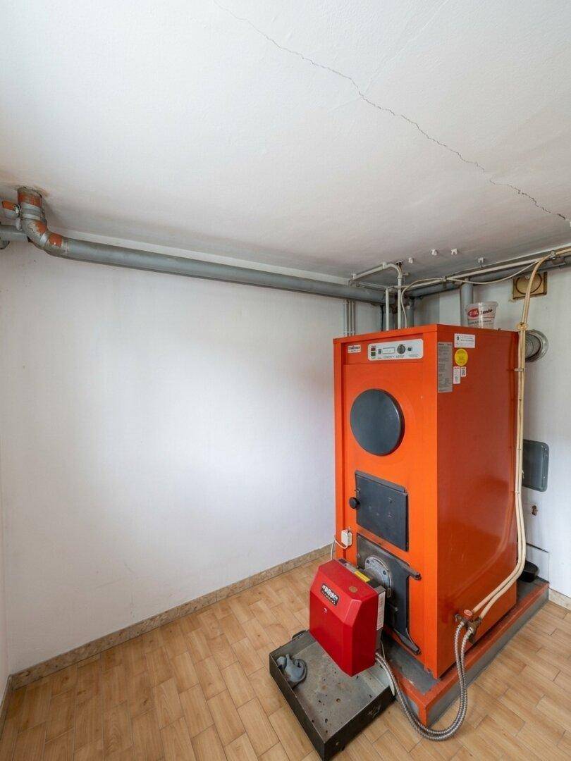 Heizungsraum im Keller mit einem großen, orangefarbenen Heizkessel und sichtbaren Leitungen.