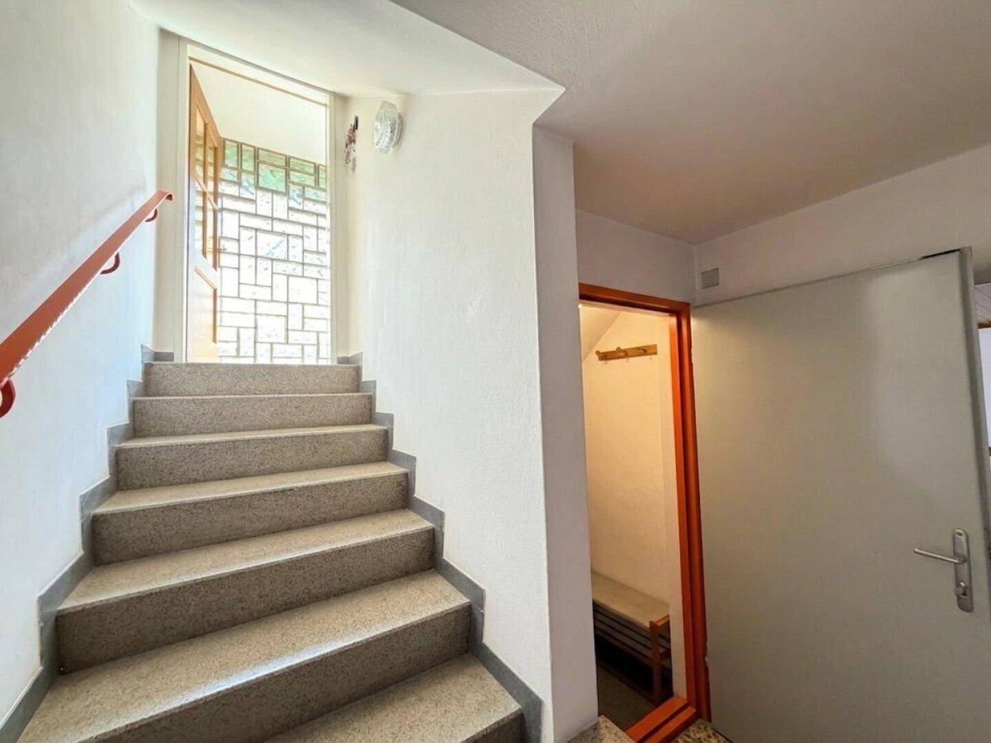 Helles Treppenhaus mit Teppichstufen und einem Fenster, das Tageslicht hereinlässt.