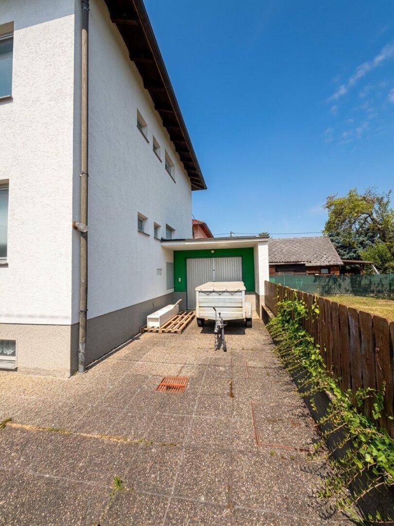 Seitenansicht eines modernen Gebäudes mit Zufahrt zur Garage und einem gepflasterten Bereich.