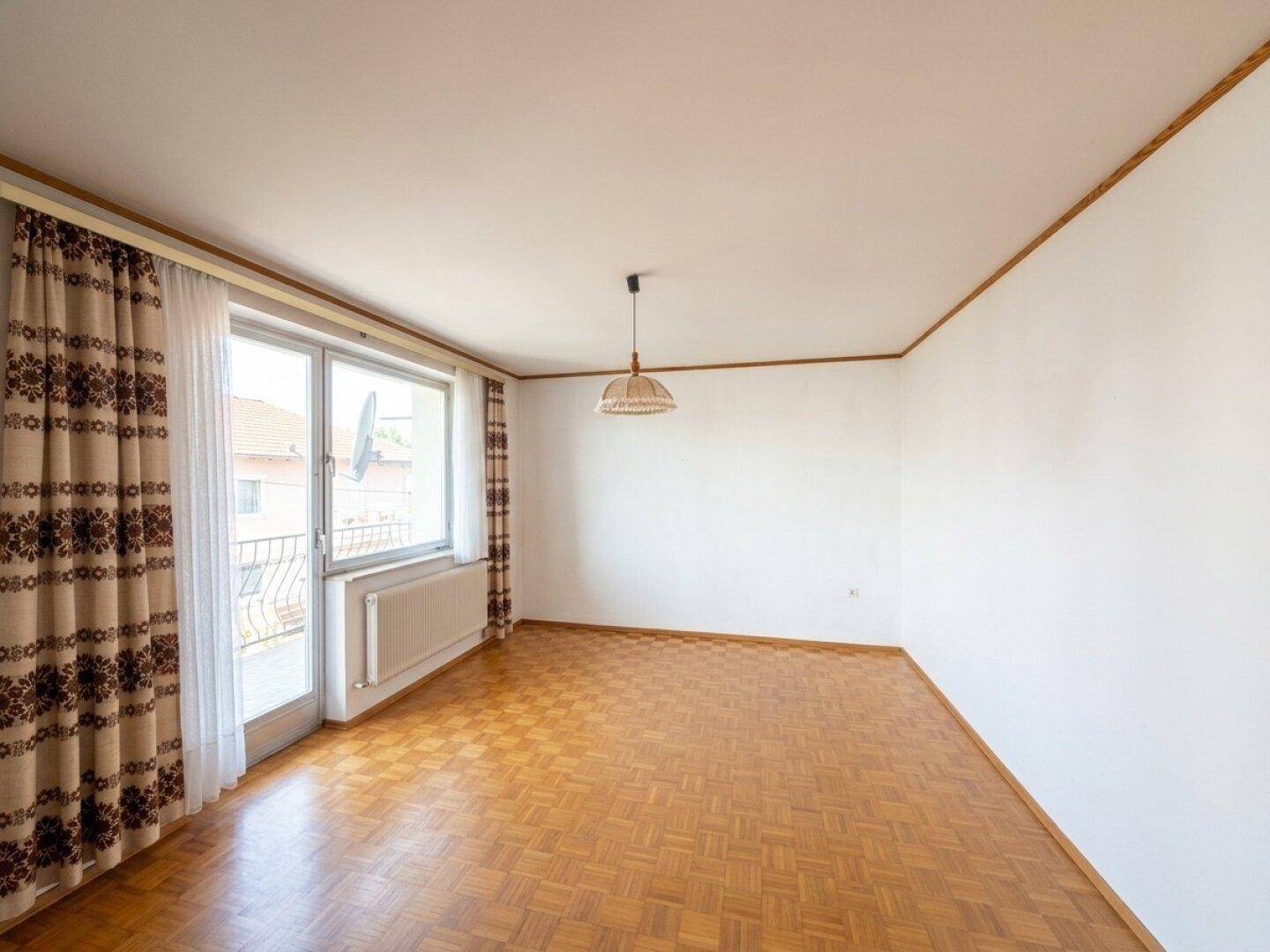 Helles Wohnzimmer mit Parkettboden, Balkonzugang und traditionellen Vorhängen.